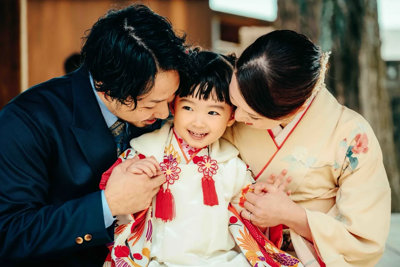 七五三の晴れ着姿のお子様を両親が笑顔で見つめる家族写真